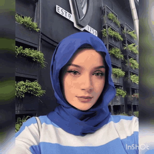 a woman wearing a blue hijab stands in front of a sign that says esto