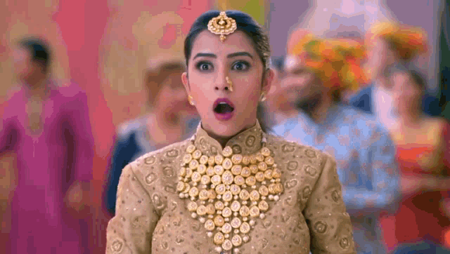 a woman wearing a gold necklace and a nose ring is standing in front of a crowd with her mouth open .