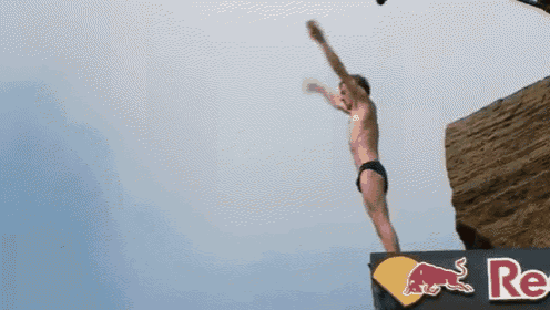 a man is jumping off a cliff with a red bull sign in the background
