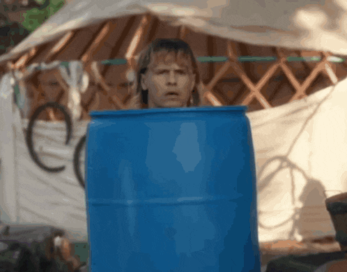 a man is sticking his head out of a blue barrel in front of a tent