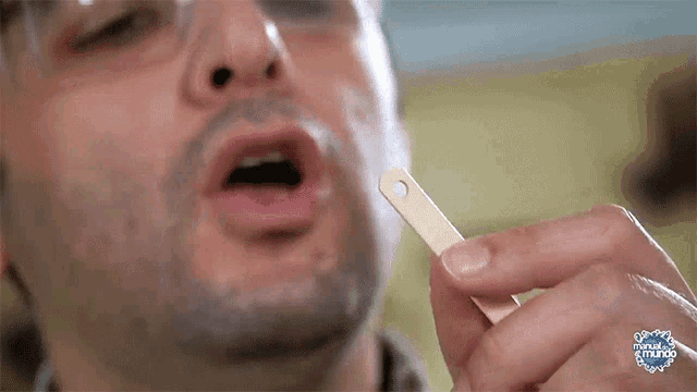 a man is holding a popsicle stick with a hole in the middle and the word mundo on the bottom right