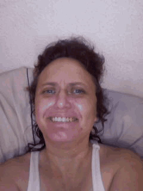 a woman in a white tank top smiles while laying on a bed