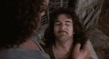 a man with long hair and a beard is laying on the ground with another man holding his neck .