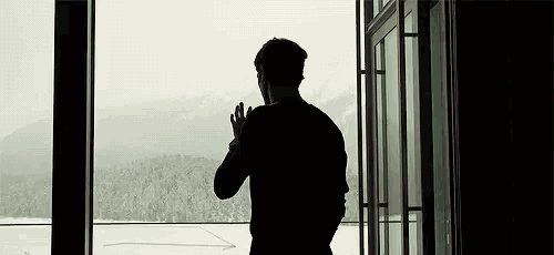 a man is standing in front of a window looking out at the mountains .