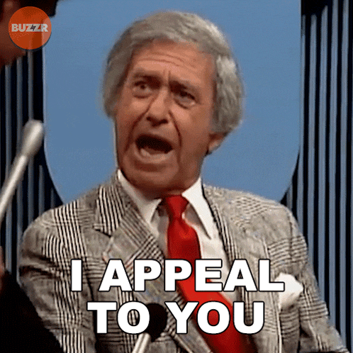 a man in a suit and tie says i appeal to you in front of a microphone