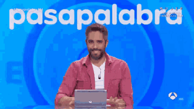 a man in a pink jacket stands in front of a blue background that says pasapalabra on it