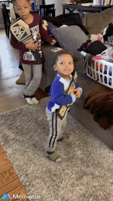 two young boys are standing in a living room and one has a wrestling championship belt on