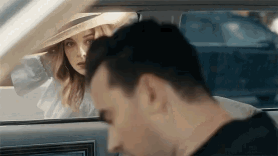 a woman in a hat is looking out the window of a car while a man looks on .