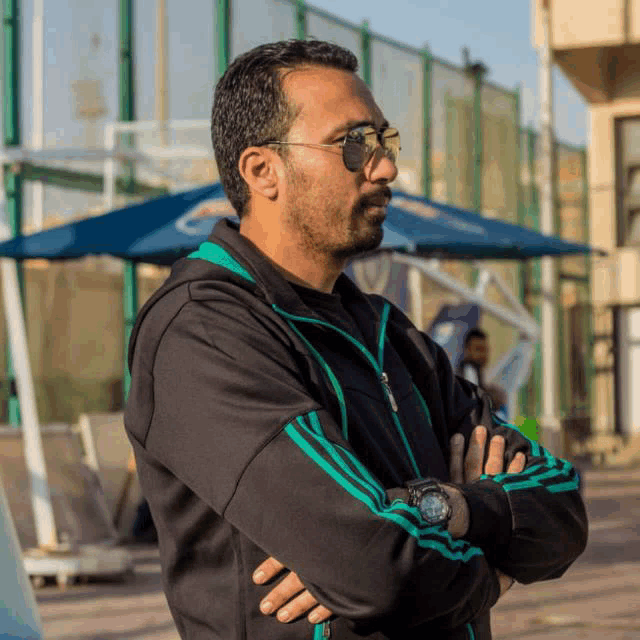 a man with his arms crossed wearing a watch and sunglasses