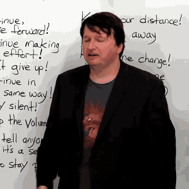 a man stands in front of a white board that says " keeping our distance "