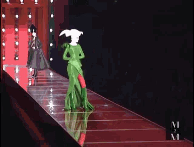 a woman in a green dress walks down the runway