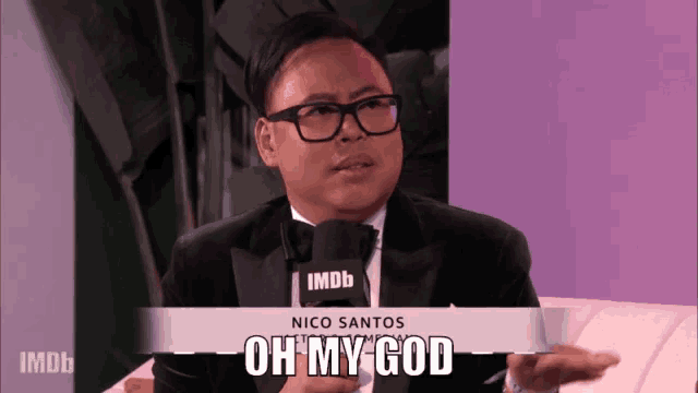 a man wearing a tuxedo and glasses is talking into an imdb microphone and says oh my god