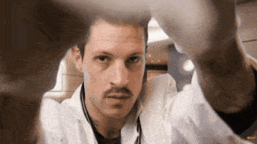 a man with a mustache and a white lab coat is looking at the camera