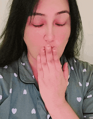 a woman covering her mouth with her hands and wearing a shirt with hearts on it