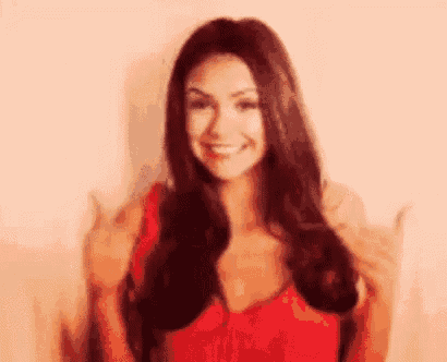 a woman in a red dress is smiling and giving a thumbs up sign .