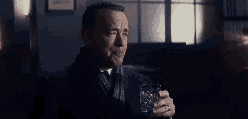 a man is holding a glass of whiskey in a dark room .