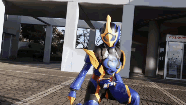 a person in a blue and yellow costume is kneeling in front of a building with a sign that says プラネタリウム
