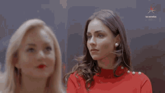 two women are standing next to each other and one is wearing a red top with pearls on the buttons .