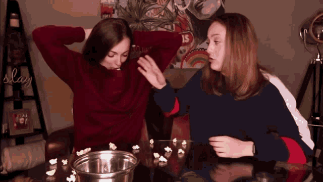 two girls are playing with popcorn and the word slay is on the wall behind them