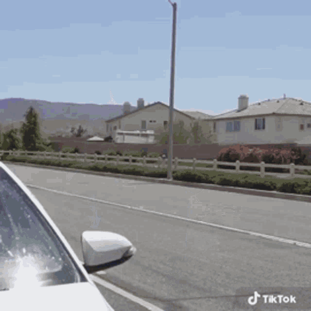 a white car is parked on the side of the road next to a white fence and houses