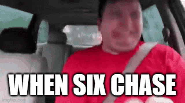 a man in a red shirt is driving a car with the words `` when six chase '' on the screen .