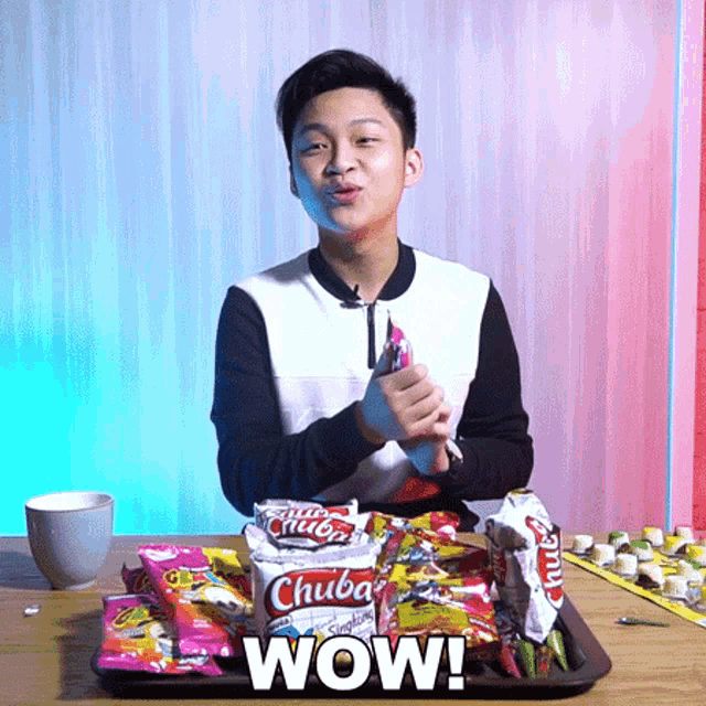 a young man is sitting at a table with a tray of chuba snacks and the words wow on the bottom
