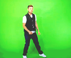 a man in a black vest and white shirt is dancing in front of a green screen