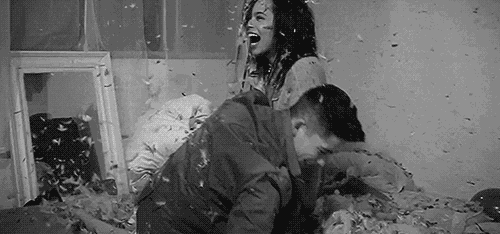 a black and white photo of a man and woman having a pillow fight on a bed .