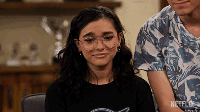 a girl wearing glasses is sitting next to a man wearing a netflix shirt