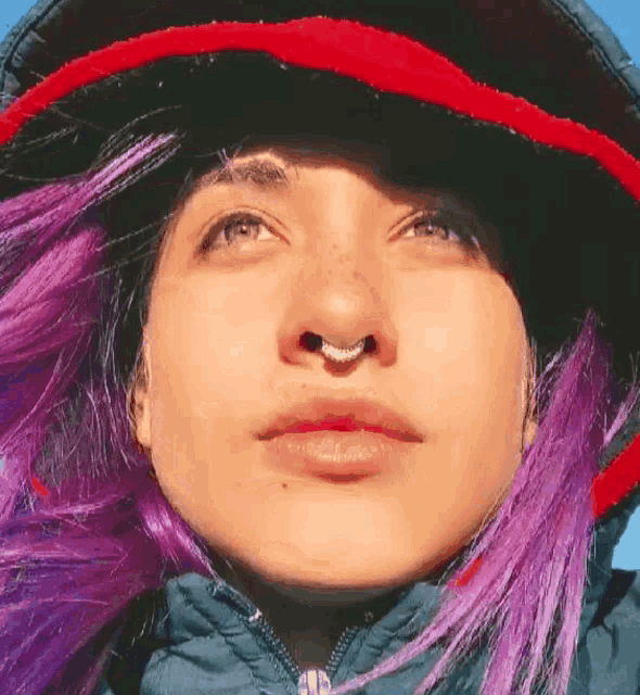 a woman with purple hair and a nose ring is wearing a red and black hat .