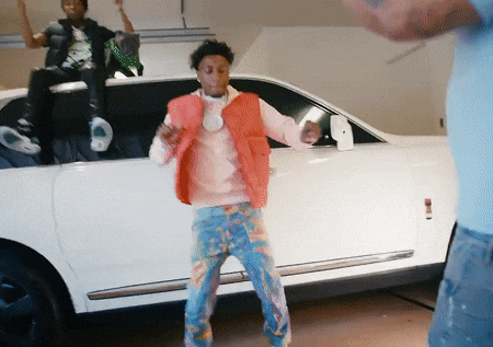 a man in a red vest is dancing in front of a white car