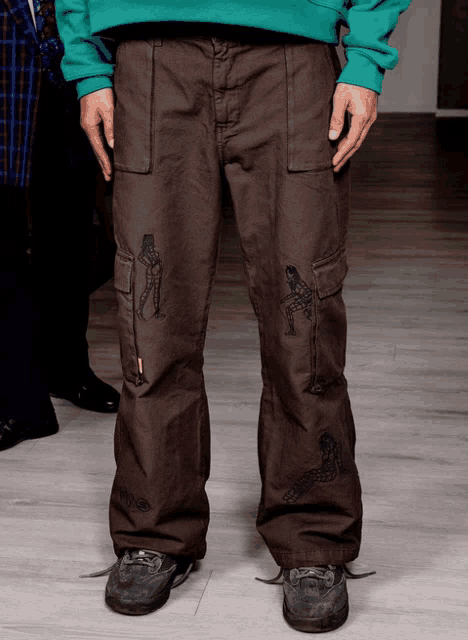 a man wearing a green sweatshirt and brown cargo pants with drawings on them