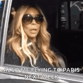 a woman wearing sunglasses is sitting in a car with her mouth open .