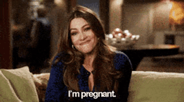 a woman is sitting on a couch and smiling and says i 'm pregnant