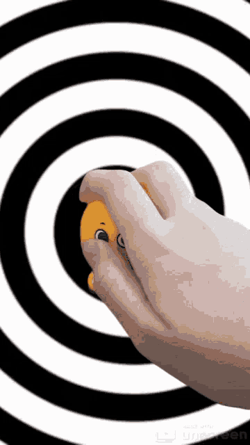 a person 's hand is holding a yellow smiley face in front of a black and white spiral