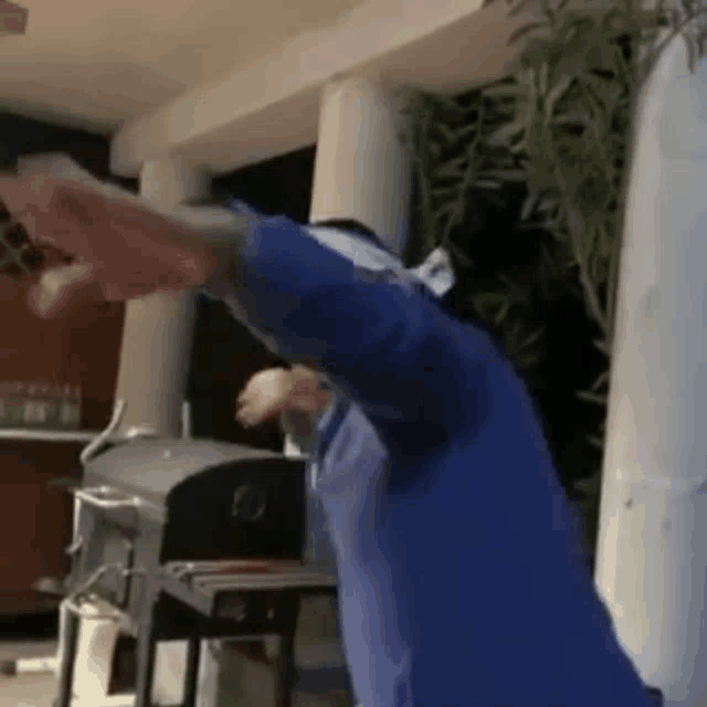 a man wearing a blue shirt is standing in front of a grill .