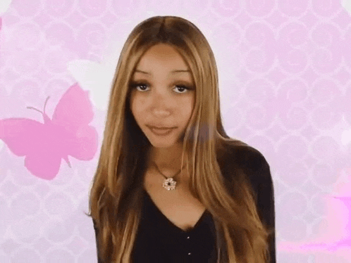 a woman wearing a black shirt and a necklace is standing in front of a pink butterfly .