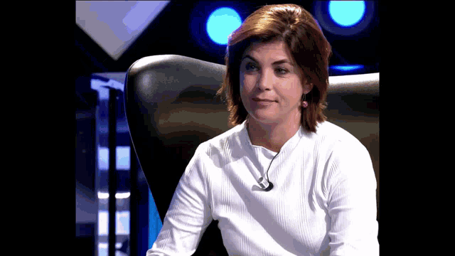 a woman in a white shirt is sitting in a chair with a microphone around her neck