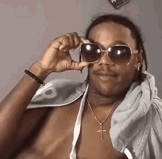 a shirtless man wearing sunglasses and a necklace with a cross on it .