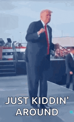 a man in a suit and tie is standing on a stage with the words just kidding around below him .
