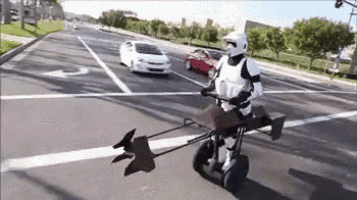 a stormtrooper is riding a segway on a street .