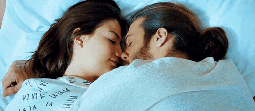 a man and a woman are sleeping in a bed and the woman is wearing a shirt that says la la