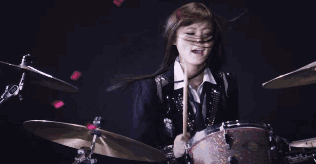 a woman playing a drum set with a drum stick in her hand