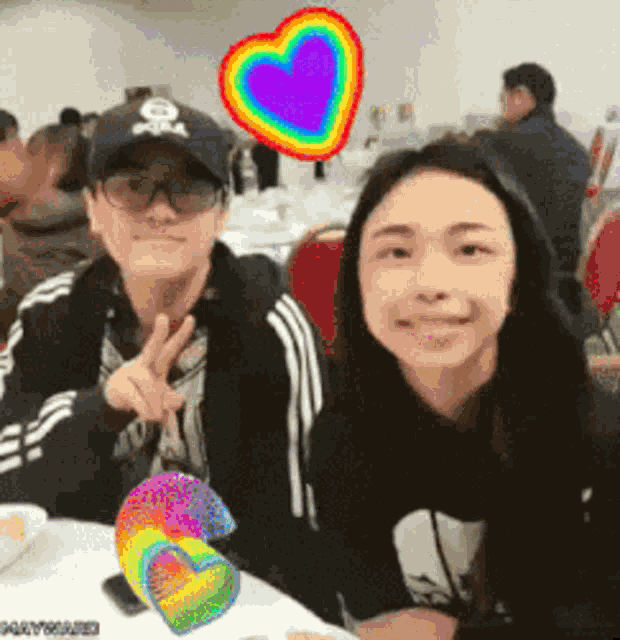 a man and a woman are posing for a picture with a rainbow heart behind them