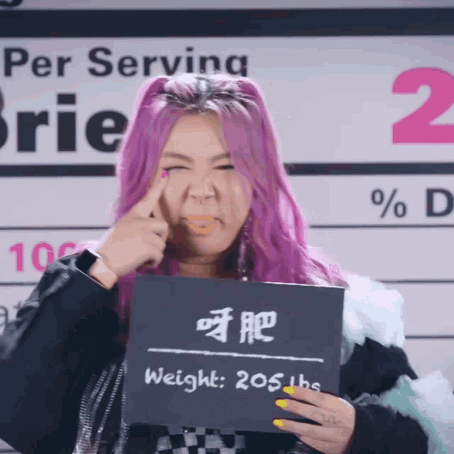 a woman with pink hair holds up a sign that says weight 205 lbs