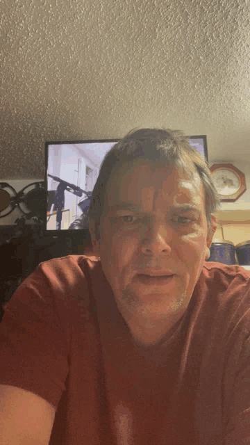 a man in a red shirt looks at the camera in front of a tv