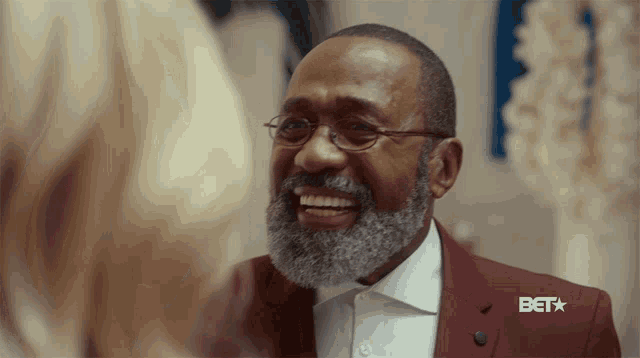 a man with glasses and a beard is smiling with a bet logo in the background