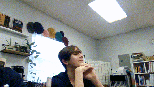 a man sits in front of a window with a clock on the wall above him