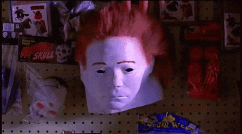 a white mask with red hair sits on a shelf next to a package of rubber skull