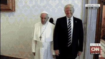 a man in a suit and tie stands next to a man in a white robe with a cross on his head